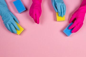 Women hands in pink and light blue rubber gloves with sponges on pink background
