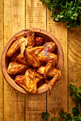 Delicious grilled chicken wings in wooden bowl with parsley on wooden table.