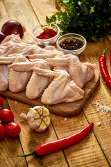 Fresh organic chicken wings on a chopping board with spices and vegetables on wooden table.