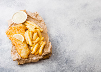 Traditional British Fish and Chips with tartar sauce on chopping board and lemon slice on white...