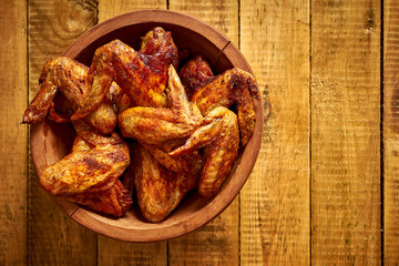 Delicious grilled chicken wings in a wooden bowl on wooden table.
