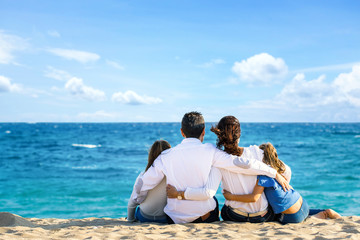 Rear view of family sitting together on beach looking at horizon.