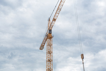 A fragment of a tower crane with a cabin on the background of a cloudy sky.