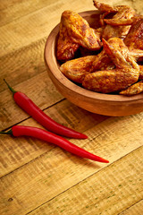 Delicious grilled chicken wings in wooden bowl with chili peppers on wooden table.