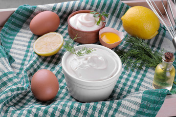 Mayonnaise in a white bowl and ingredients for making mayonnaise on a green napkin. white sauce.