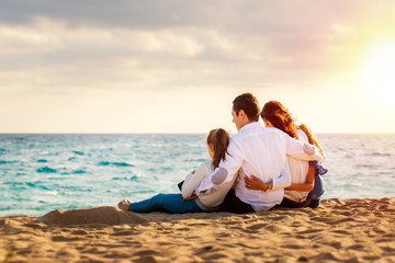 Young family sitting together in late afternoon sun on beach.