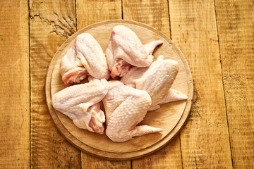 Fresh organic chicken wings on chopping board on old wooden table.
