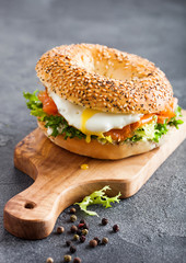 Fresh healthy bagel sandwich with salmon, ricotta and soft egg on vintage chopping board on stone kitchen table background. Healthy diet food.