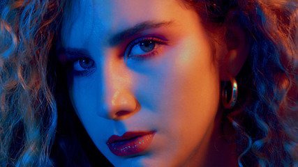 closeup portrait of blonde woman with curly hair in blue-red light wears 90th style makup