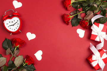 Rose flowers with alarm clock, gifts and decorative hearts on red background. St. Valentines Day...