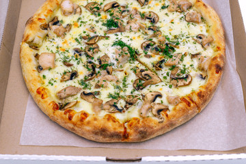 Pizza in a cardboard box on a light background. Top view. Pizza delivery. Pizza menu. Pizza on the kitchen table.