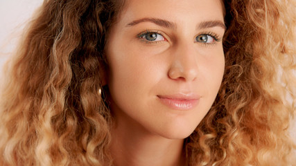 happy smiling, flirty glance closeup portrait of blonde model with ideal skin and cyrly hair
