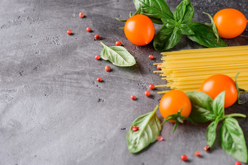 Spaghetti, tomatoes, basil and pepper on a concrete surface. With copy space.