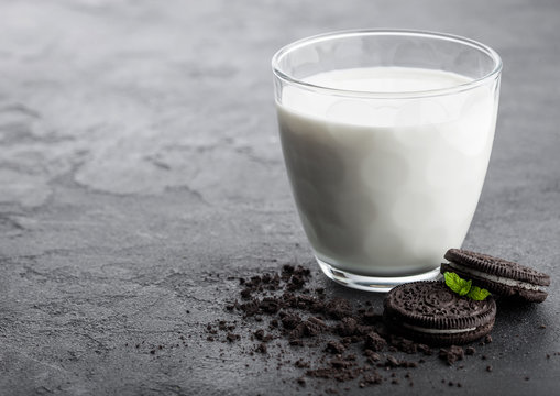 Glass of milk and black sandwich cookies on black stone kitchen table background. Space for text.