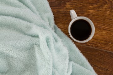 Blanket and black coffee on wooden background