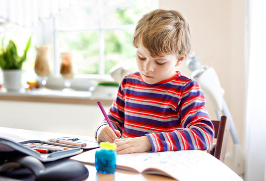 Happy smiling little kid boy at home making homework at the morning before the school starts. Little child doing excercise, indoors. Elementary school and education: Boy drawing geometric figures