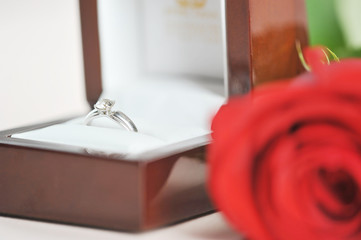 Ring with a diamond in a gift box. Next to the box is a red rose. The perfect holiday gift. Light background. Close-up. Macro shooting.