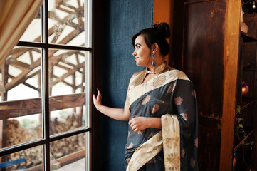 Elegant brunette south asian indian girl in saree posed indoor cafe against window.