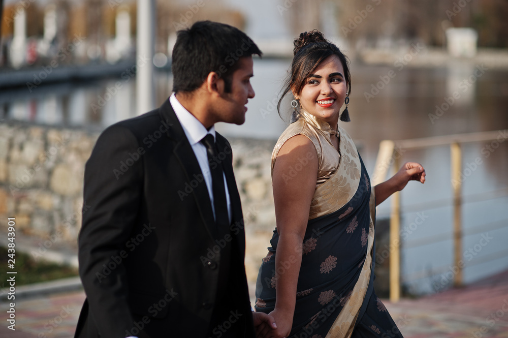 Wall mural Elegant and fashionable indian friends couple of woman in saree and man in suit walking together and holding hands.