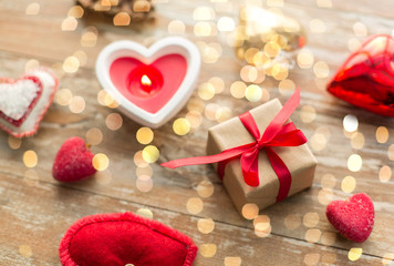 christmas, valentines day and holidays concept - gift box with heart shaped decorations and candle burning on wooden background