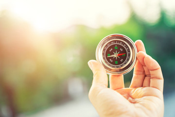 Closeup of hand holding compass with blurred green nature and sunlight with flare background with free copy space for text. Life, travel and guide for success concept.