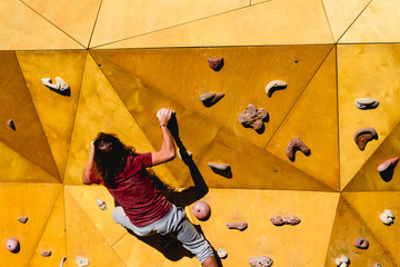 Male climber trying a complicated route to the sun on an outdoor climbing wall