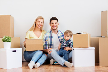 Fototapeta na wymiar mortgage, people, family and real estate concept - happy mother, father and little son with cardboard boxes moving to new home
