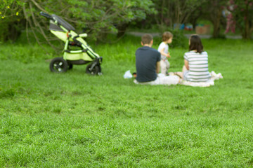 Obraz na płótnie Canvas Defocused young parents with baby sitting on a green grass in park in far and selective focuse on a grass in foreground