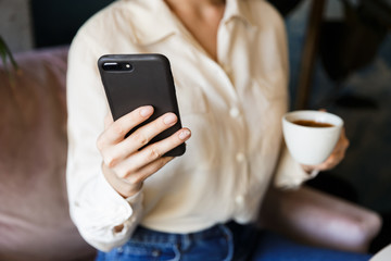 Beautiful young woman sitting in cafe indoors work drinking coffee using mobile phone.