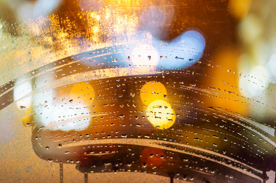 Blurry night city lights in the rain as seen through a damp windshield of the car with water droplets