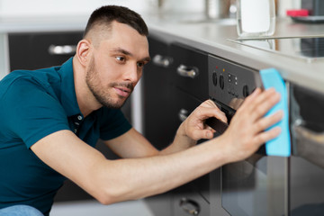 household and people concept - man wiping table with cloth cleaning oven door at home kitchen