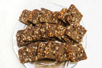 Pieces of bread with sunflower seeds, rye bran in white plate on white background.