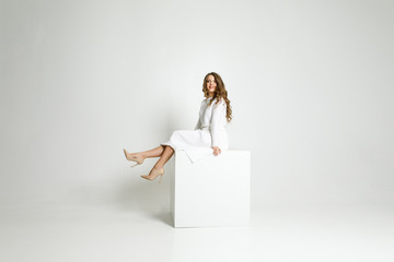 young beautiful girl in white clothes standing in a white room on a white cube