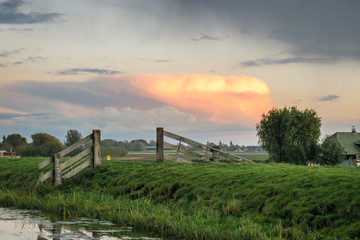 Panorama of a distant autumn storm in The Netherlands illuminated by the light of the setting sun. Scenic view of the dutch countryside with sunlit clouds in the distance.
