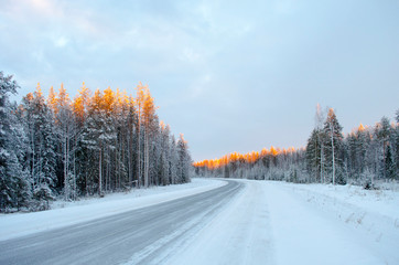 Northern winter road lit by the rays of the setting sun
