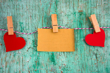 old blank paper and paper red hearts hung on clothespins on a rope on a mint green wall background