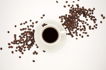 Weiße Tasse mit schwarzem Kaffee und einer Untertasse zwischen Kaffeebohnen. Ansicht von oben, isoliert auf weißem Hintergrund