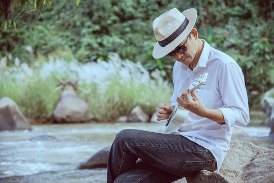 Man play ukulele new to the river- people and music instrument life style in nature concept