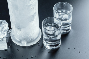 Cold vodka in shot glasses on a black background.