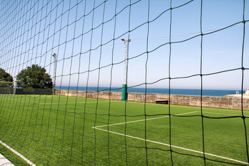 Look through net to empty football field in soccer stadium. Soccer field with green grass in football sport stadium behind net curtain. Sport equipment, football goal, white line, soccer field corner.