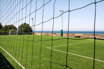 Look through net to empty football field in soccer stadium. Soccer field with green grass in football sport stadium behind net curtain. Sport equipment, football goal, white line, soccer field corner.
