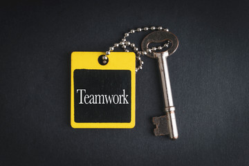 TEAMWORK inscription written on wooden tag and key on black background with selective focus and crop fragment. Business and education concept
