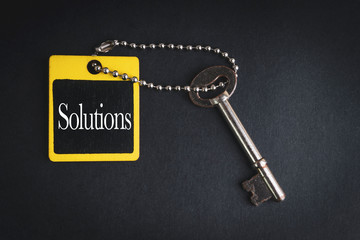 SOLUTIONS inscription written on wooden tag and key on black background with selective focus and crop fragment. Business and education concept
