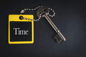 TIME inscription written on wooden tag and key on black background with selective focus and crop fragment. Business and education concept