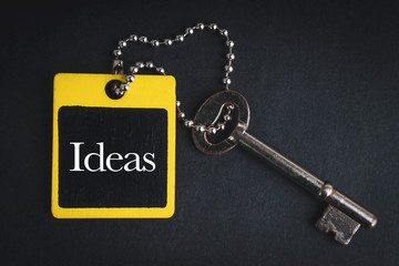 IDEAS inscription written on wooden tag and key on black background with selective focus and crop fragment. Business and education concept