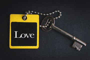 LOVE inscription written on wooden tag and key on black background with selective focus and crop fragment. Business and education concept