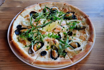 Seafood pizza with mussels, squid and shrimps, topped with olives, onion, herbs and lemon