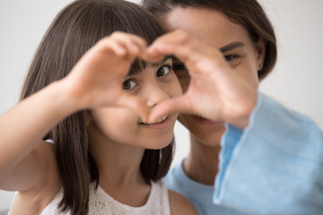 Portrait of little happy girl and mother join hands forming heart shape as concept of giving love, child mum connection unity, cute kid daughter and mom bonding looking at camera, child care adoption