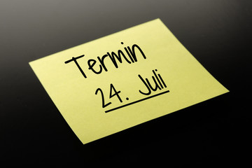 Termin 24. Juli - gelber Notizzettel dunkler Hintergrund