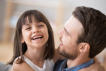 Adorable funny kid girl laughing looking at camera embracing happy father, smiling little daughter...